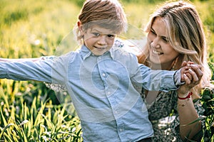 Happy young mother looks with love at her son 3 years old, close-up portrait outdoors among the grass