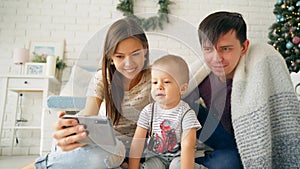 A happy young mother makes taking selfies of her family. Young parents with a young son are photographed on a smartphone