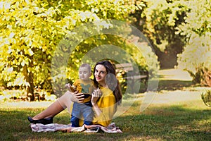 Happy young mother playing with baby in autumn park with yellow maple leaves. Family walking outdoors in autumn. Little boy with h