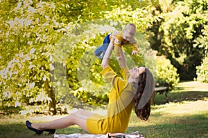 Happy young mother playing with baby in autumn park with yellow maple leaves. Family walking outdoors in autumn. Little boy with h