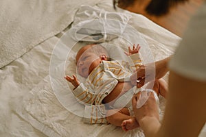 Happy young mother playing with baby while changing his diaper on bed.