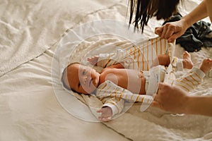 Happy young mother playing with baby while changing his diaper on bed.