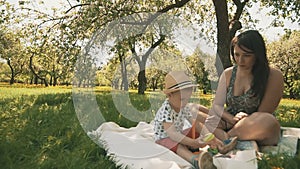 Happy young mother playing on blanket with her adorable son under tree at park