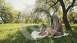 Happy young mother playing on blanket with her cute son under tree at park