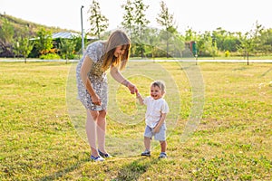 Happy young mother playing with her little baby son on sunshine warm autumn or summer day. Beautiful sunset light in a