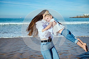 Happy young mother plays with her cute kid on the beach, laughing and turning around, leaving footstep on the wet sand