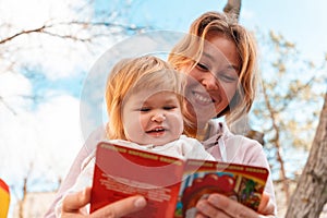 Happy young mother reads a book to her little daughter while relaxing in the park. Bottom view. The concept of