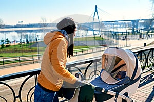 A happy young mother smiles and walks with a stroller and a child on the street to the park. Communication and leisure