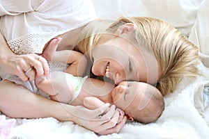 Happy Young Mother Snuggling Newborn Baby Daughter in Bed