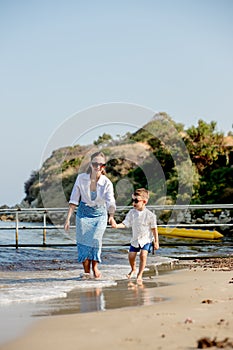 Happy young mother with son on a sunny day running by the sea. Rest on the beach. A happy family