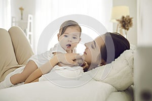 Happy young mother together with her sweet adorable baby cuddling on bed at home