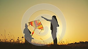 Happy young mother and two children playing with a kite while on meadow at sunset. Funny family time.