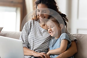 Happy young mother watching funny cartoons on computer with daughter.