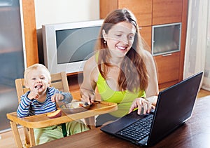 Happy young mother working with laptop and baby
