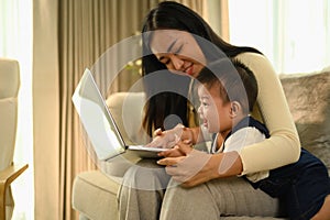 Happy young mother working remotely on laptop while taking care of her baby