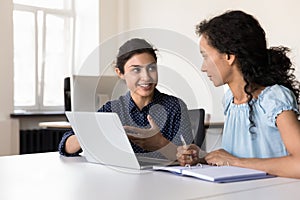 Happy young multiethnic businesswomen talking at laptop