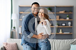 Happy young multiracial couple holding home keys and hugging