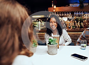 Happy young multiracial group of friends in casual clothing laughing with drinks by table at bar
