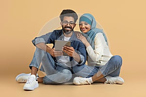 Happy young muslim couple sitting closely and looking at digital tablet together