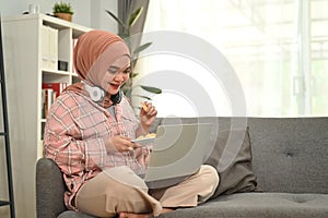Happy young muslim woman wearing hijab with a happy face using laptop computer on couch at home