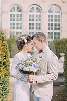 Happy young newlyweds embracing near the old beige house with columns and big vintage windows. Romantic wedding in Paris