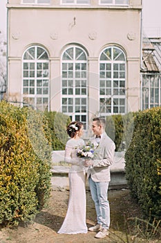 Happy young newlyweds embracing near the old beige house with columns and big vintage windows. Romantic wedding in Paris