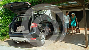 Happy young newlyweds walk out of their home to pack their luggage in the SUV.