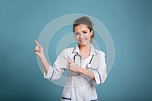 Happy young nurse with stethoscope pointing