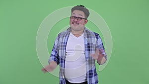 Happy young overweight Asian hipster man waving hand