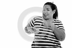 Happy young overweight Asian woman pointing at fresh vegetable wrap while sticking tongue out