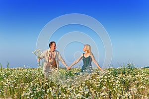 The happy young pair in the field of chamomiles.Portrait in a sunny day