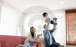 Happy young parents Caucasian father and Asian mother playing with little kid girl by holding cute baby fly in the air