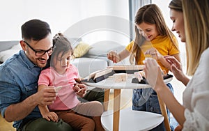 Happy young parents and children having fun, playing board game at home