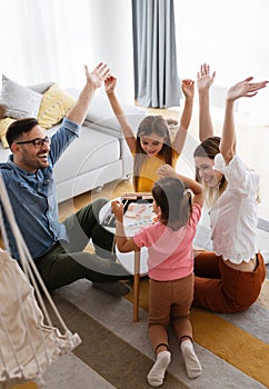 Happy young parents and children having fun, playing board game at home