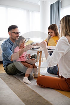 Happy young parents and children having fun, playing board game at home