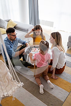 Happy young parents and children having fun, playing board game at home