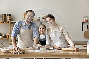 Happy young parents and girl in aprons baking together