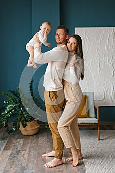 Happy young parents hold their little son in their arms and smile happily at the camera