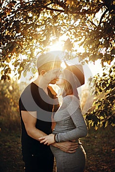 Happy young parents, mom and dad, hugging baby bump, enjoying beautiful moment at sunset. Stylish pregnant couple holding hands on