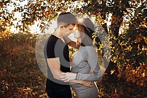 Happy young parents, mom and dad, hugging baby bump, enjoying beautiful moment at sunset. Stylish pregnant couple holding hands on