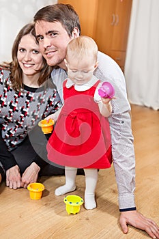 Happy young parents playing with their baby daughter on floor