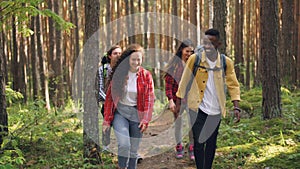 Happy young people in casual clothing are trekking in forest walking along path, talking and laughing enjoying nature