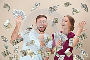 Happy young people with money and falling American dollars on beige background