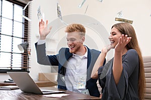 Happy young people playing online  using laptop under money rain in office