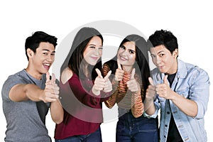 Happy young people show thumbs up on studio
