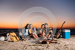 happy young people smiling at camera while sitting together on sandy beach