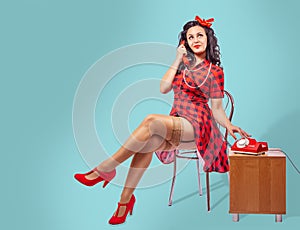 Happy young pinup woman sitting on a chair and talking on phone