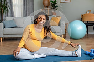 Happy young pregnant african american woman with big belly doing exercises and practicing yoga in living room