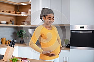 Happy young pregnant african american woman touching her big belly and feeling baby move