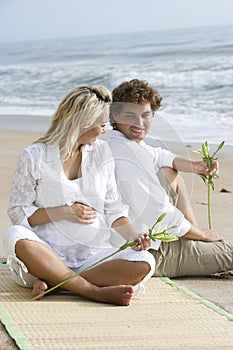 Happy young pregnant couple relaxing on beach